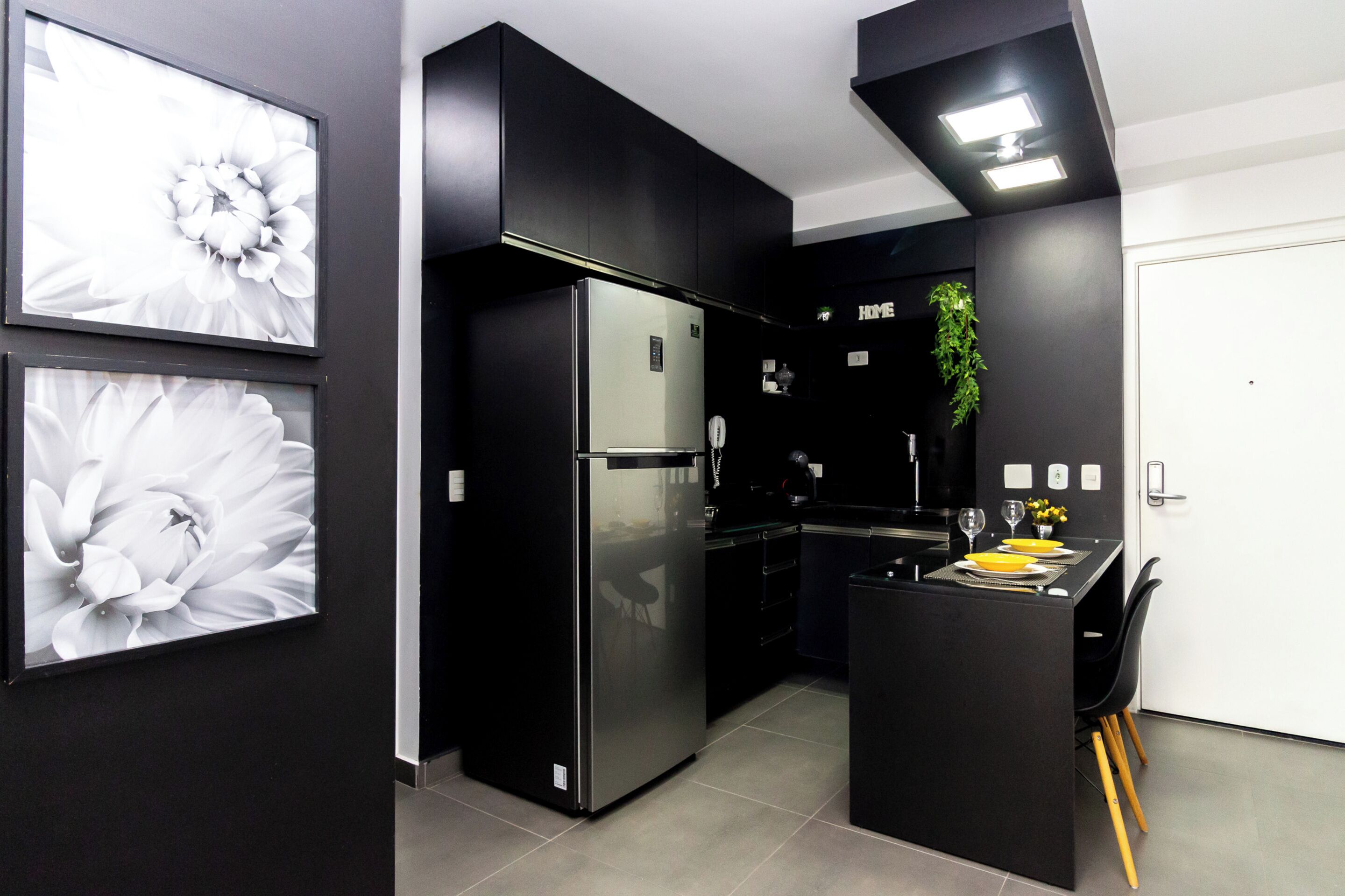 A modern kitchen with black cabinetry, a built-in refrigerator, and a small dining area with a table and chairs.