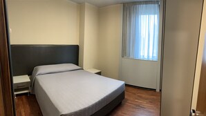 A bedroom with a bed, a nightstand, a window with curtains, and a door. - Residence Castelli - Trilocale 1 (Montecchio Maggiore-Alte Ceccato)