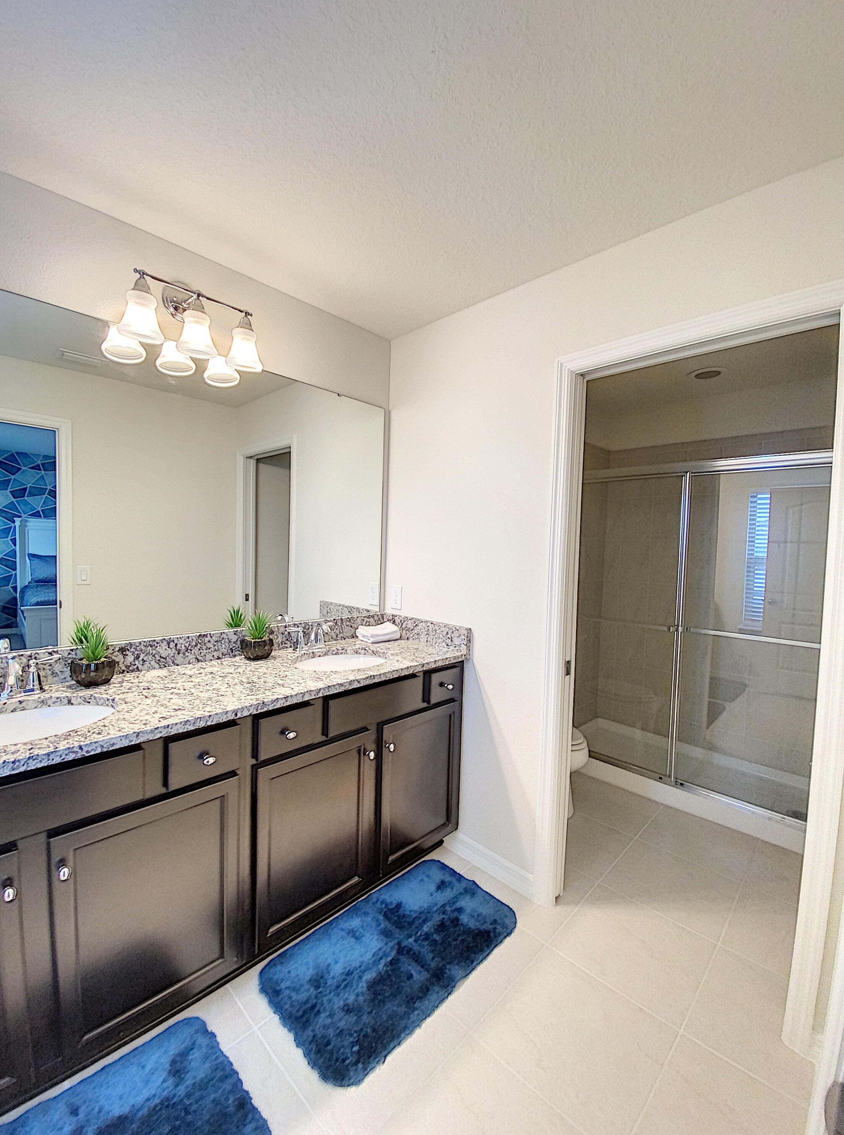 A modern bathroom with a large vanity, a shower enclosure, and a blue rug.