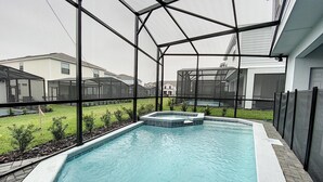 Una piscina con un recinto in vetro, circondata da un cordolo in mattoni e da un prato.