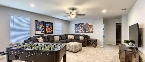 A living room with a foosball table, a sectional sofa, and a ceiling fan.