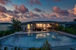 A swimming pool with a patio area, a covered outdoor kitchen, and a view of the sky.