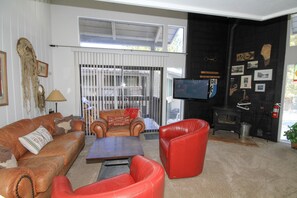 Un salon avec un canapé en cuir marron, un fauteuil en cuir rouge, une table basse en bois et un téléviseur posé sur un meuble.