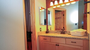 A bathroom with a granite countertop, a sink, a mirror, and wooden cabinets. - Sierra Park Villas #82 (Mammoth Lakes)