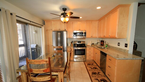 A kitchen with wooden cabinets, stainless steel appliances, a dining table with chairs, and a ceiling fan. - Sierra Park Villas #82 (Mammoth Lakes)