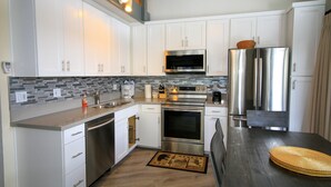A modern kitchen with white cabinets, stainless steel appliances, and a wooden dining table. - Sierra Park Villas #93 (Mammoth Lakes)