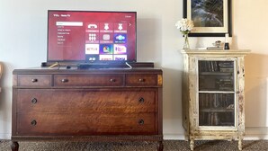 Un téléviseur à écran plat posé sur un meuble en bois, avec un tableau encadré au-dessus.