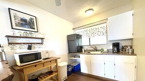 Une cuisine compacte avec des meubles blancs, un four à micro-ondes, un évier et une machine à café.