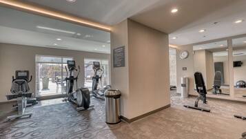 Un gimnasio con equipo de ejercicio, un bote de basura y un reloj en la pared.