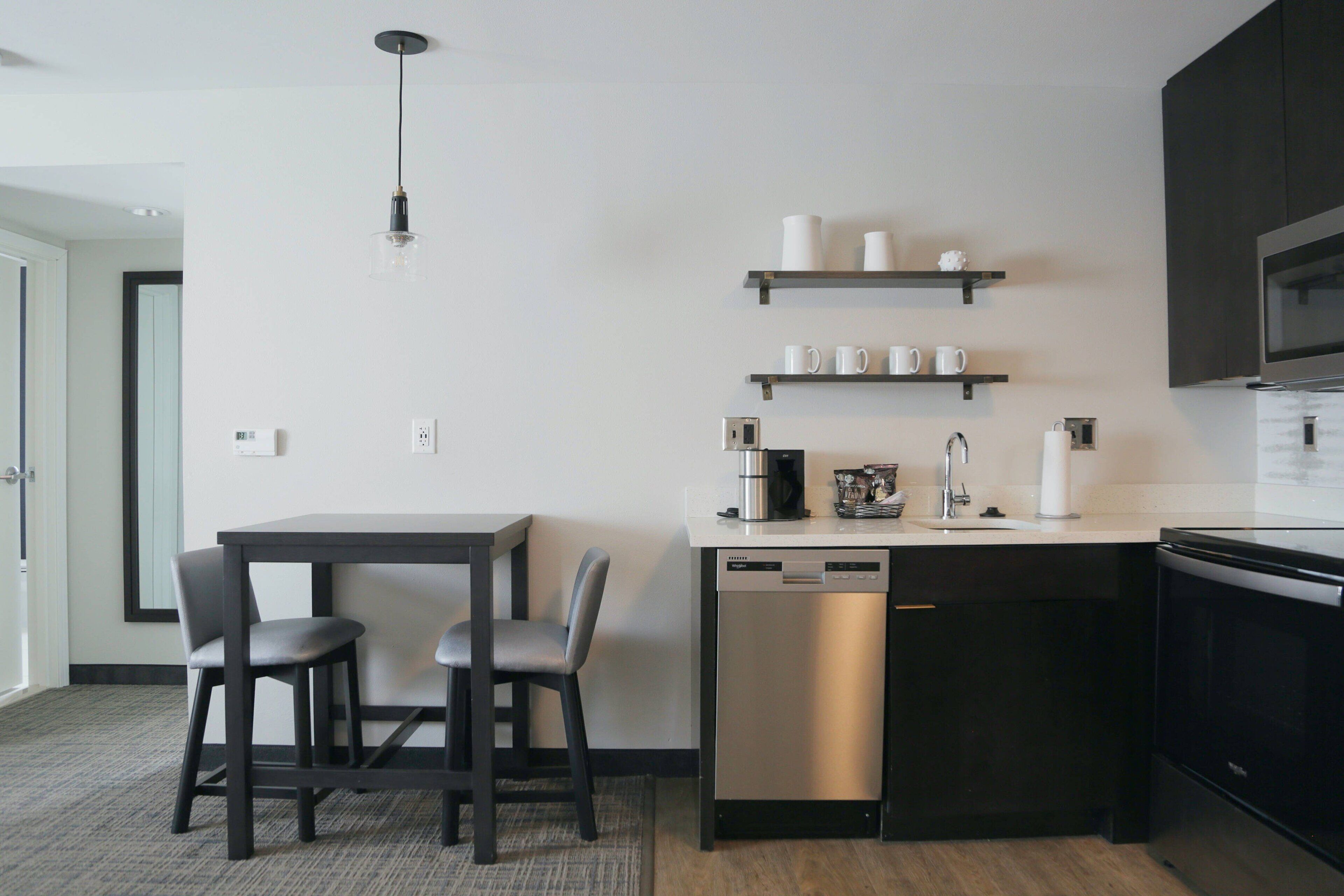 A modern kitchen with a dishwasher, a coffee maker, and a microwave. There are two chairs and a table.
