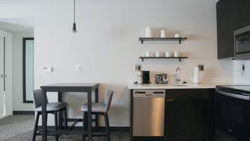 A modern kitchen with a dishwasher, a coffee maker, and a microwave. There are two chairs and a table.
