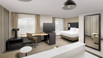 A hotel room with a bed, a desk, a television, a chair, a small table, and a large mirror.