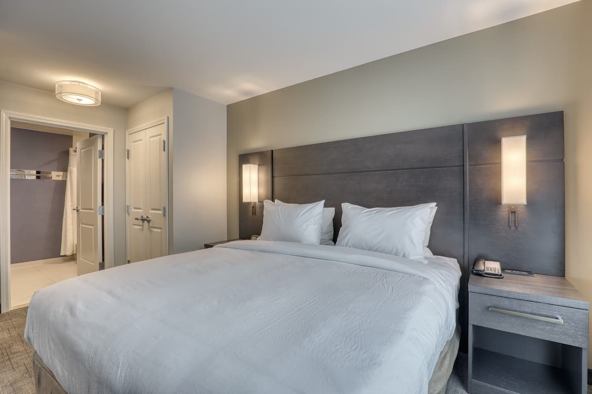 A hotel room with a large bed, bedside lamps, a nightstand, and a door leading to a bathroom.