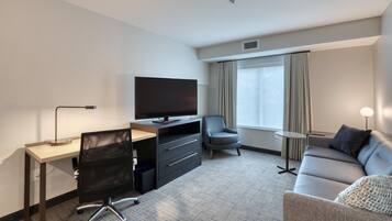 A modern hotel room with a desk, chair, television, sofa, and a small table.
