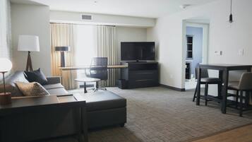 Una habitación de hotel moderna con sofá, una pequeña mesa, televisión y zona de comedor.