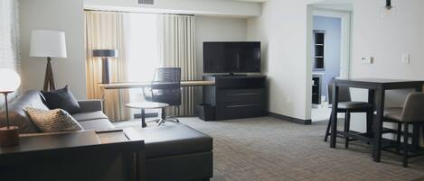 Une chambre d’hôtel moderne équipée d’un canapé, d’une petite table, d’une télévision et d’un coin repas.
