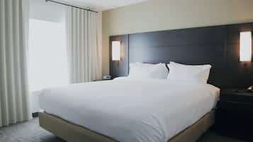 A hotel room with a large bed, a dark headboard, bedside lamps, a nightstand, and a window with curtains.