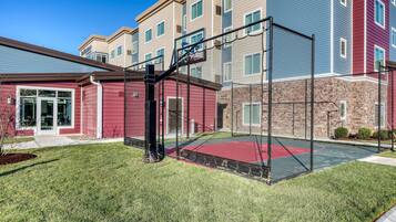 A basketball court with a net, surrounded by a building with multiple windows and a red exterior.