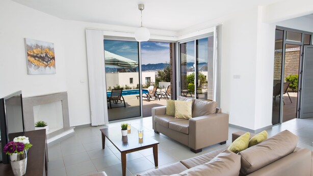 Ein modernes Wohnzimmer mit einer Couch, einem Couchtisch und einem Kamin. Im Hintergrund ist ein Pool und eine Berglandschaft zu sehen.