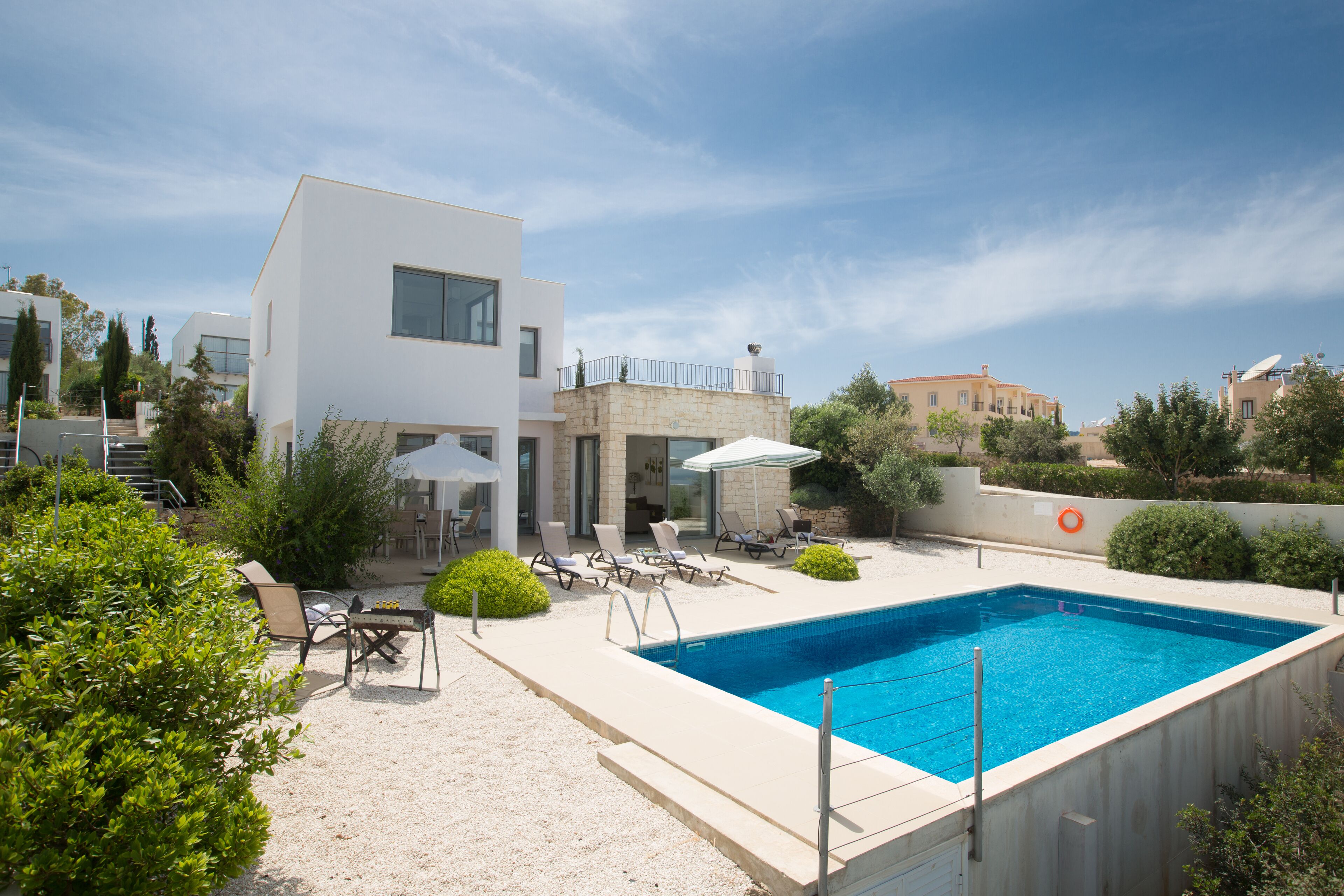Un área de piscina moderna con una piscina rectangular, sillas de descanso y sombrillas.
