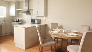 Een moderne keuken met witte kastjes, een magnetron en een fornuis. Er is een eethoek met een houten tafel en stoelen.