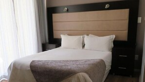 Een hotelkamer met een groot bed, een hoofdeinde, twee nachtkastjes en een raam met gordijnen.