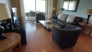 Een moderne hotelkamer met een bank, fauteuil en een bijzettafeltje. Er is een balkon met uitzicht op de stad.