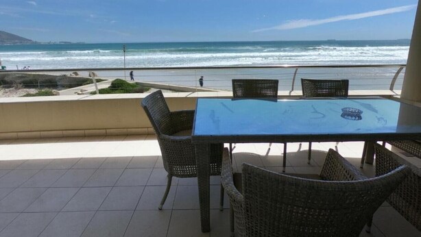 Een terras met een tafel en stoelen, uitkijkend op het strand.
