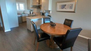 Een compacte keuken met een centraal kookeiland, een eettafel met vier stoelen, en een lijst met een afbeelding aan de muur.