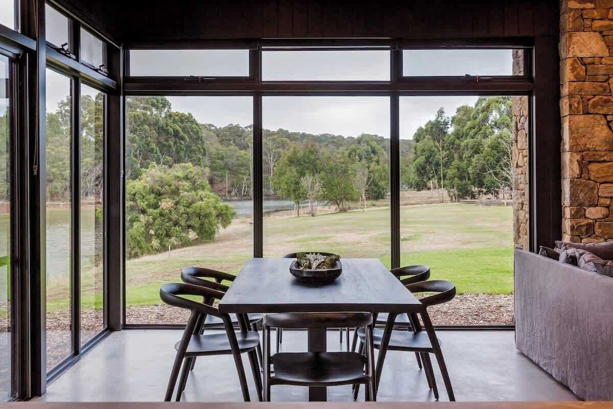 A dining area with a table and chairs, large windows with a view of a green landscape.