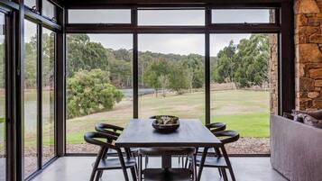 A dining area with a table and chairs, large windows with a view of a green landscape.