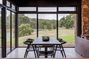 A dining area with a table and chairs, large windows with a view of a green landscape.