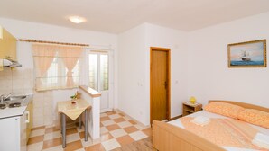 Een kleine, schone kamer met een bed, een bureau, een raam met gordijnen, een deur en een schilderij aan de muur.