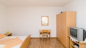 Un dormitorio con cama, escritorio, silla, armario, televisor y ventana con cortina.