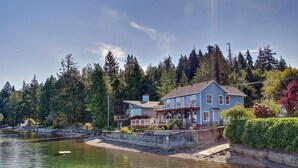 A two-story house with a dock extending into a calm lake, surrounded by dense forest. - Hood Canal waterfront five bedrooms hottub watercrafts boat launch Olympic view (Belfair)