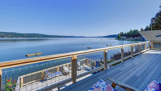 A wooden deck with a railing, overlooking a calm lake with boats, surrounded by trees and a distant shoreline. - Hood Canal waterfront five bedrooms hottub watercrafts boat launch Olympic view (Belfair)