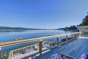 A wooden deck with a railing, overlooking a calm lake with boats, surrounded by trees and a distant shoreline. - Hood Canal waterfront five bedrooms hottub watercrafts boat launch Olympic view (Belfair)