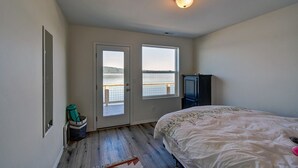 A bedroom with a bed, a wardrobe, a small cabinet, a window with a view of the water, and a door leading to an outdoor area. - Hood Canal waterfront five bedrooms hottub watercrafts boat launch Olympic view (Belfair)
