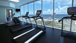 A gym with treadmills and a stationary bike, large windows with a beach view, and an American flag. - San Carlos 1001 (Gulf Shores)