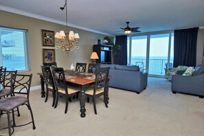 A living room with a dining table, chairs, a sofa, and a balcony with a view. - San Carlos 1001 (Gulf Shores)
