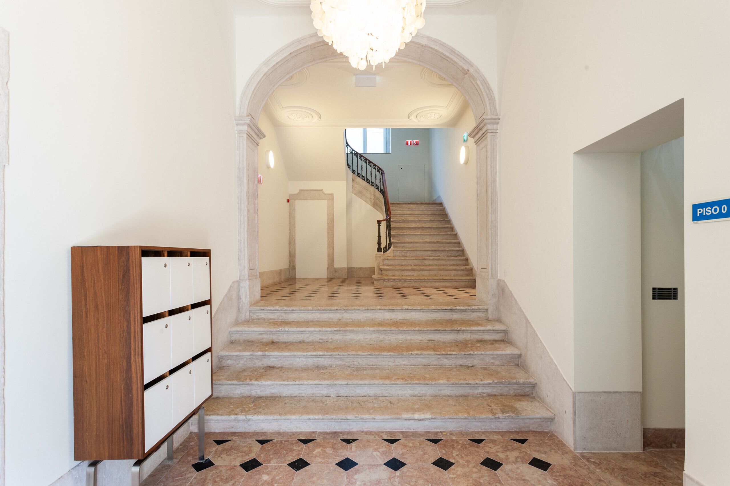 Una escalera con piso estampado que conduce a una plataforma, un mueble de madera con cajones y un cartel que indica 'PISO 0'.