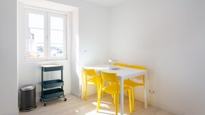 Une pièce lumineuse avec une table blanche et des chaises jaunes, une fenêtre et un chariot en métal.