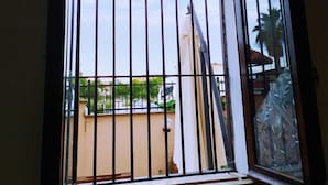 A window with metal bars, a view of a building with a white facade, and a clear sky. - Vailletta Fiorita (Rome)