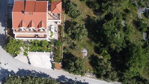 Vue aérienne d’une maison avec un toit recouvert de tuiles rouges, une terrasse avec des meubles d’extérieur et une zone boisée environnante.