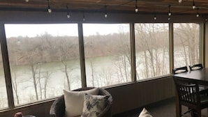A cozy room with a large window overlooking a river, furnished with a sofa and chairs.