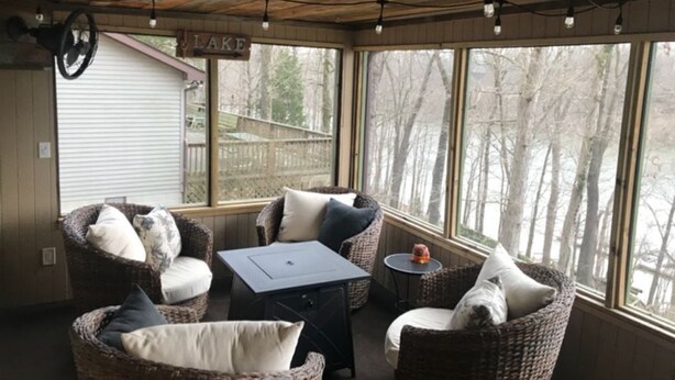 A cozy room with wicker furniture, a table, and large windows offering a view of trees.