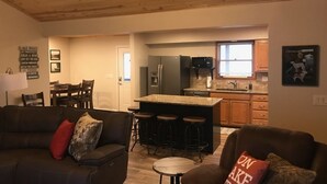 A cozy living room with a wooden ceiling, a kitchen with a bar area, and a dining area.