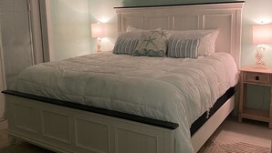 A bedroom with a large bed, two bedside lamps, a painting above the bed, and a window with blinds. - 2BR/2BA - Availability now! 
- Clean
- Close to the beach
 - Sleeps 6 (Mexico Beach)