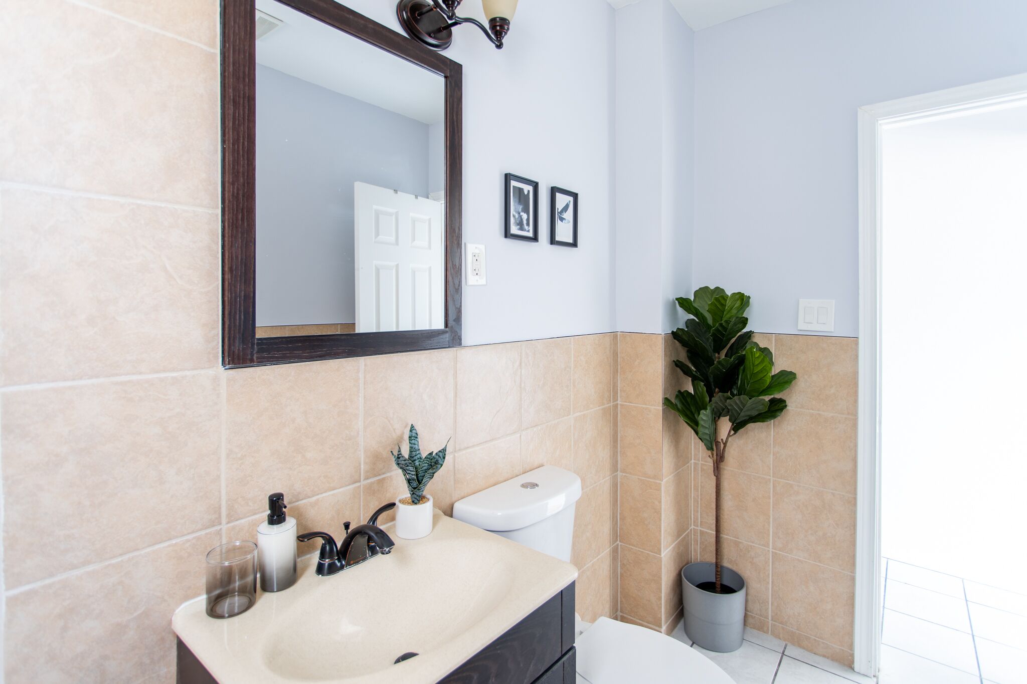 Une salle de bain équipée d’un lavabo, d’un miroir, de toilettes et de deux tableaux encadrés accrochés au mur.