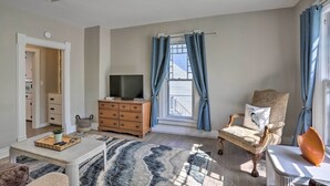 Una sala de estar con televisor, una silla, una mesa y una ventana con cortinas.